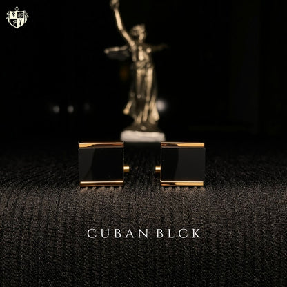 A pair of men's cufflinks with rectangular black enamel faces and gold-toned edges, displayed on a dark textured surface with a blurred gold statue in the background. The text 'CUBAN BLACK' is visible at the bottom.